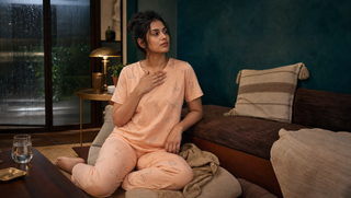 Synthetic South Asian woman in peach Sweet Dreams-style pyjamas seated in a teal monsoon lounge, illustrating how a racing pulse can keep sleep away.
