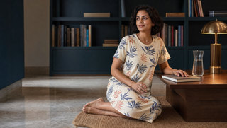 Synthetic Indian woman in a cream botanical Sweet Dreams-style nightdress seated in a teal study-library morning pause, illustrating how brain fog can have a night-time cause.