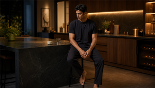 Synthetic man in Sweet Dreams Mellow Tone Henley Pyjama Set seated at a late-evening kitchen island, illustrating how caffeine can hide the body's tired signal.