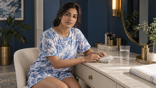 Synthetic woman in blue printed sleepwear at a morning vanity, noticing signs of a restless night