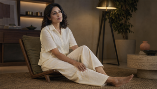 Synthetic woman in Sweet Dreams Linen Edit Button Down Palazzo Pyjama Set seated low in a walnut and sage reading lounge, illustrating how heavy legs can keep sleep shallow.