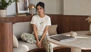 Homewear for women blog thumbnail: a synthetic South Asian woman in a Sweet Dreams cream and sage coord set sits front-facing in a walnut breakfast nook beside a closed laptop and tea cup.