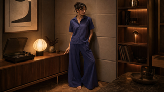 Woman in indigo linen Sweet Dreams pyjama set beside a record console in a warm listening room