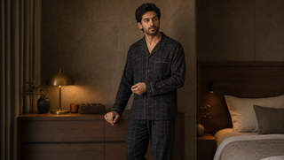 What do most men wear to bed blog thumbnail: a synthetic South Asian man in a dark Sweet Dreams button-front pyjama set stands beside a walnut dresser in warm lamplight.