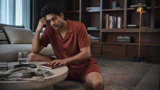 Synthetic Indian man in a rust wave-print Sweet Dreams-style shorts set seated in a dawn library lounge, illustrating how restless nights can trick your memory.