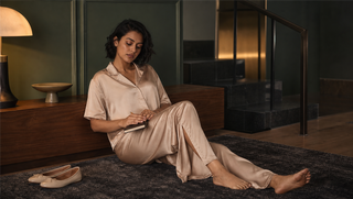 Synthetic woman in a champagne Sweet Dreams satin pyjama set seated on a moss-and-charcoal stair landing after evening practice, illustrating how sleep continues the brain's learning work.