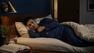 Synthetic Indian man in a navy micro-wave Sweet Dreams-style button-down pyjama set sleeping on his side in a blue-hour bedroom, illustrating how snoring can steal sleep in tiny pieces.