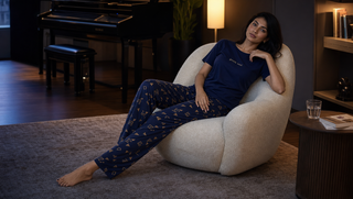 Synthetic South Asian woman in Sweet Dreams navy Gentle Soul pyjama set reclining in a modern music room as evening light softens and the body winds down for sleep