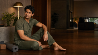 Synthetic Indian man in tea-leaf Sweet Dreams-style henley pyjama set seated after evening stretching, illustrating how the body learns while asleep.