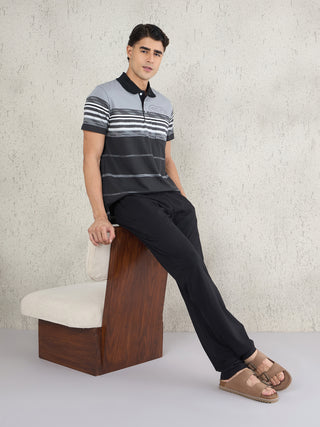 Men sitting on a chair wearing a black and grey striped polo shirt and black pants.