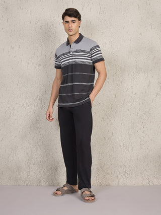 Men standing, wearing a black and grey horizontally striped polo shirt and black pants.