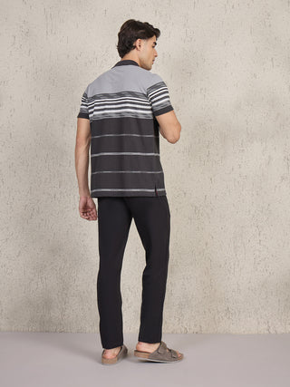 Men standing, wearing a black and grey horizontally striped polo shirt and black pants.