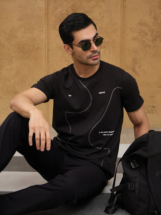 A man in black sleepwear with a graphic print poses casually on steps.