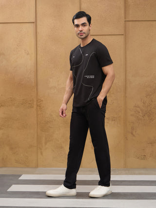 Men, standing, wearing a black t-shirt with white graphic print and black pants.