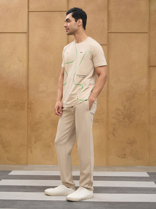 Men's light beige t-shirt with green abstract print and matching pants, posed standing on a crosswalk.