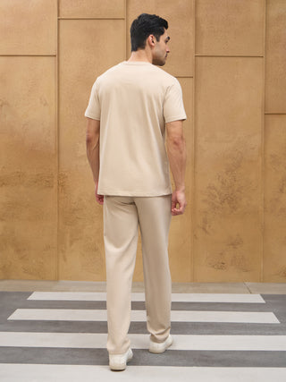 Men's light beige t-shirt with green abstract print and matching pants, posed standing on a crosswalk.
