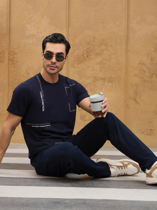Men wearing navy blue printed t-shirt and navy blue pants, sitting down holding a cup.