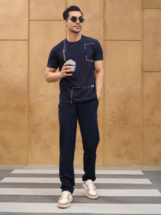 Men walking across a crosswalk, wearing a navy blue graphic t-shirt and navy blue pants.