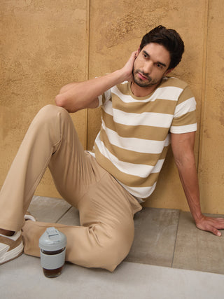Men's striped t-shirt and beige pants, sitting casually with a travel mug, similar to the previous image but with a different pose.