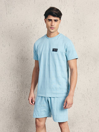 Men's light blue plaid pajama set with a short-sleeved top featuring a chest logo.