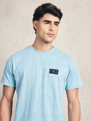 Men wearing a light blue, textured t-shirt with a dark blue patch on the chest.