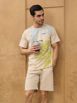 Men's beige loungewear set with a marble print t-shirt and matching shorts, holding a travel mug.