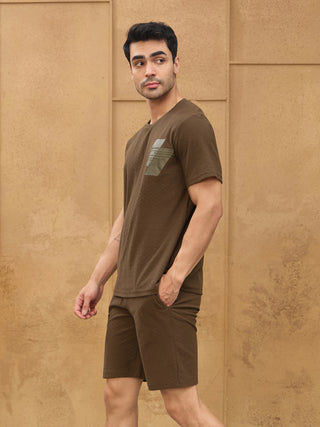 A man in a brown textured t-shirt and shorts with a pocket detail, looking away from the camera.