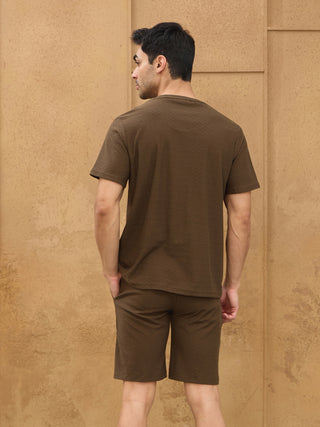 Men in a brown textured t-shirt and shorts with hands in pockets.