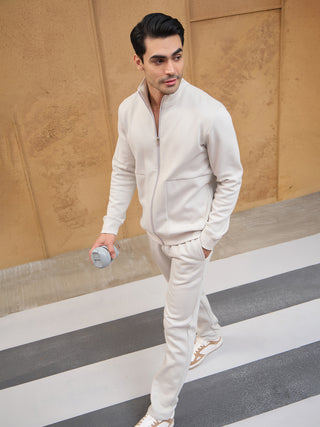 A man in a cream-colored, zip-up track suit walks while holding a grey water bottle.