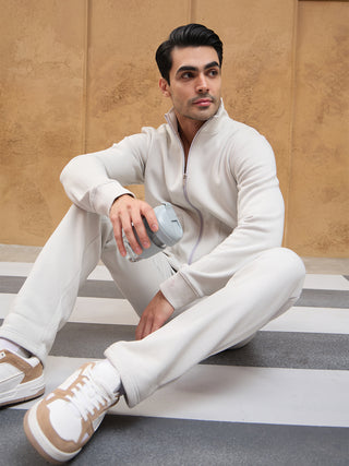 A male model sits wearing a light grey zip-up tracksuit.