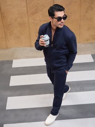 A man in a navy blue tracksuit walks across a crosswalk holding a travel cup.