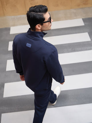 Men walking across a crosswalk wearing a navy blue zip-up sweatshirt and matching pants.