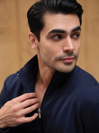 Men's navy zip-up sleepwear jacket with collar, with hand on chest, looking to the side.