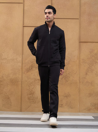 A man in a black zip-up jacket and pants walks forward, hands in his pockets.