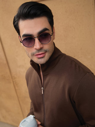A man in a brown zipped jacket holds a light blue bottle.