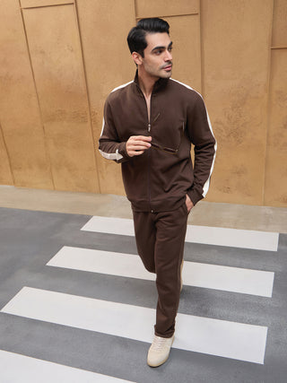 A man in a brown tracksuit with white stripes on the sleeves walks across a crosswalk.