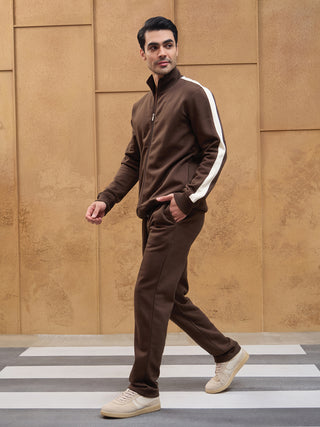Men in a brown tracksuit with white stripes on the sleeves walking on a crosswalk.