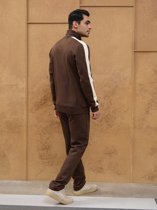 Men wearing brown sweatpants and a brown sweatshirt with white stripes walking, with the sweatshirt having a high neckline and the sweatpants having a relaxed fit.