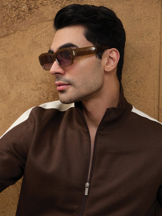 Men in a close-up shot wearing a brown zippered track jacket with cream stripes on the shoulders, featuring a textured background.