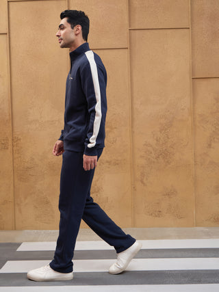 Men in a dark blue tracksuit, with a white stripe detail on the sleeve, walking across a crosswalk.