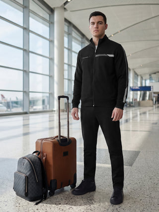 A man in a black tracksuit poses with luggage at an airport.