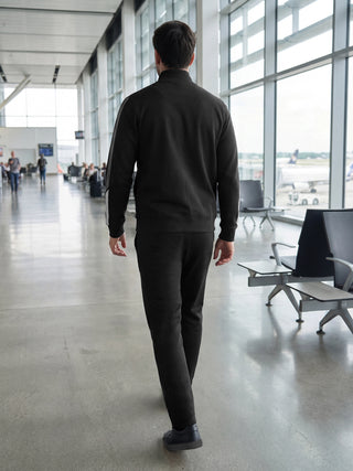 Men walking in a black tracksuit in an airport.