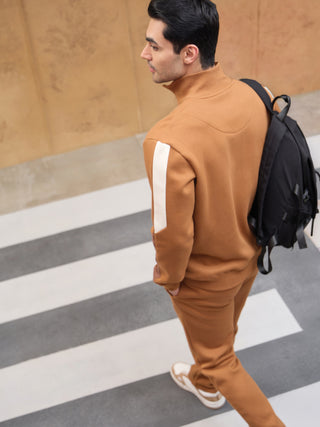 Men wearing a tan tracksuit with white stripe accents and a black backpack walking on a crosswalk.