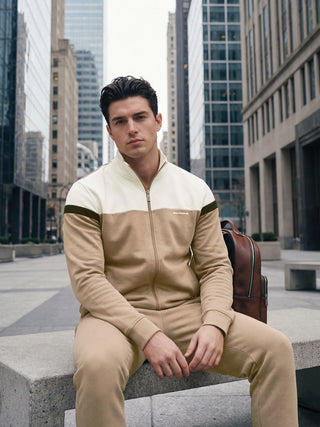 A man wearing a cream and tan tracksuit with a leather backpack.
