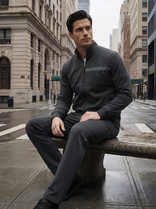 A man wearing a dark grey tracksuit sits on a stone bench outdoors on a rainy day.