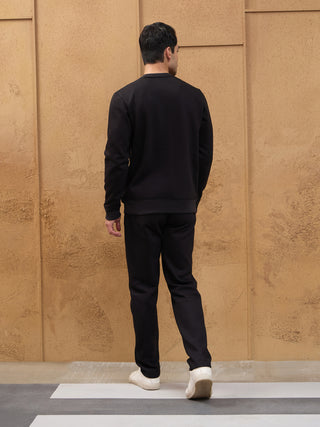 Men wearing a black crewneck sweatshirt and black sweatpants, seen from behind, walking on a crosswalk.
