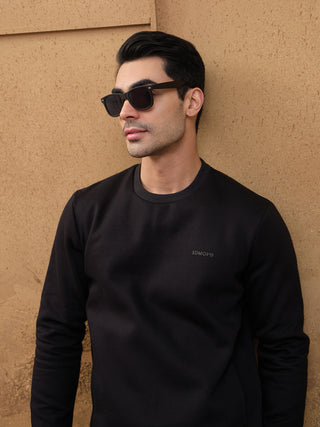 Men wearing a black crewneck sweatshirt and black sweatpants, seen from behind, walking on a crosswalk.