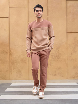 A man walks wearing a brown two-piece loungewear set with a contrasting upper chest panel, different from the previous image which showed a similar set but in a lighter shade of brown.