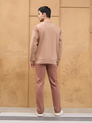 Men, standing facing away, wearing a light brown sweatshirt with darker brown shoulder accents and matching brown sweatpants.