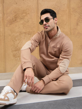 Men in a relaxed pose wear a tan quarter-zip sweatshirt with elbow patches and matching sweatpants.